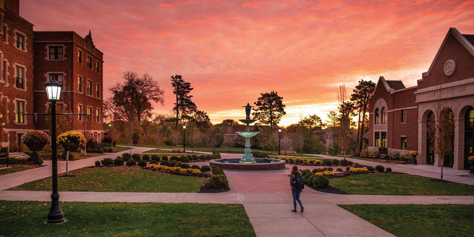 A student walks through the Academic Quad at sunset